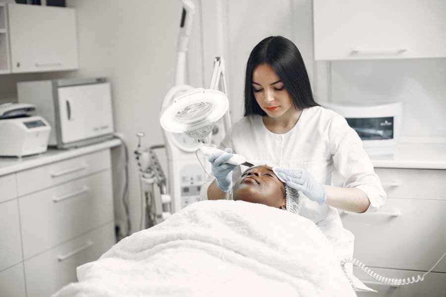 Esthéticienne réalisant un soin du visage en cabine, la cliente allongée sous la lampe